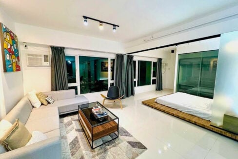 Open living space flowing to a raised wooden platform bed by the corner windows