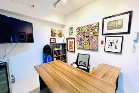 Home office with an L-shaped wood desk, mesh chair, bookshelf and wall-mounted TV