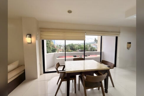 Dining area with floor-to-ceiling glass doors to a balcony overlooking trees and the hills