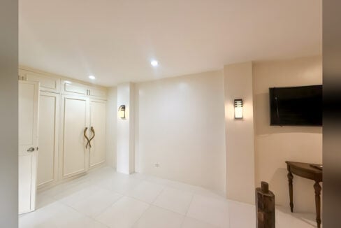 Built-in cream wardrobes with brass handles and wall-mounted TV in the bedroom