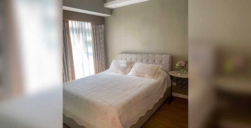 Bedroom with tufted headboard in a furnished 1BR condo for rent at Solinea