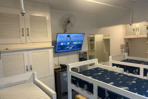 Studio with bunk beds, a wall-mounted TV, wall fan and louvered storage cabinets