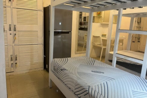 Lower bunk beside the lockers and two-door refrigerator, with the kitchenette reflected in the mirror