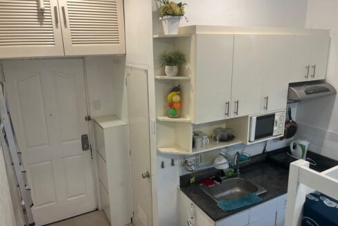 Kitchenette with white cabinets, a granite counter, stainless sink and range hood beside the entry