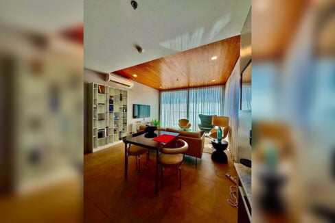 Living and dining area with wood-plank ceiling and white bookshelf in a 2BR corner condo for rent at The Reef, Mactan