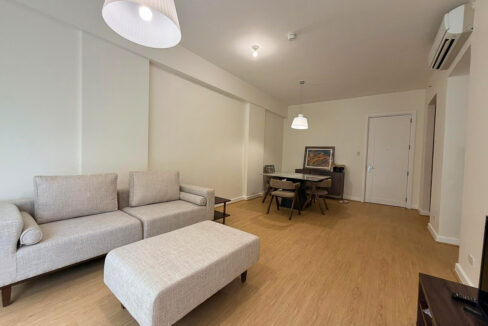 Cream fabric sofa and ottoman under a pleated white pendant lamp, with split-type aircon above