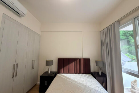 Bedroom with a burgundy tufted headboard, built-in wardrobe and a window onto the greenery