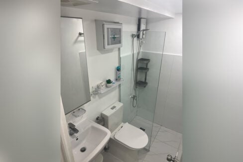 Bathroom with a glass shower panel, water heater, toilet and pedestal sink