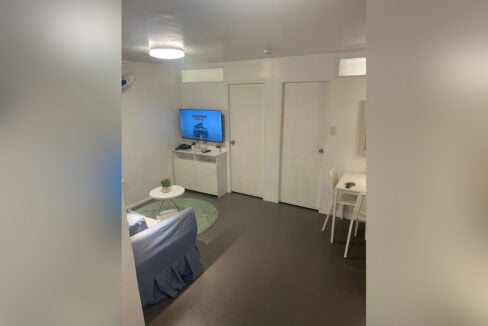 Living area with a wall-mounted TV on a custom-built console and the two bedroom doors