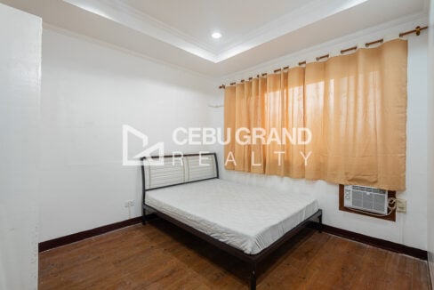 Bedroom with a metal-frame bed, peach curtains and window-type air conditioning