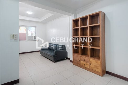 Sitting area with a black leather sofa, timber bookshelf and window-type air conditioning