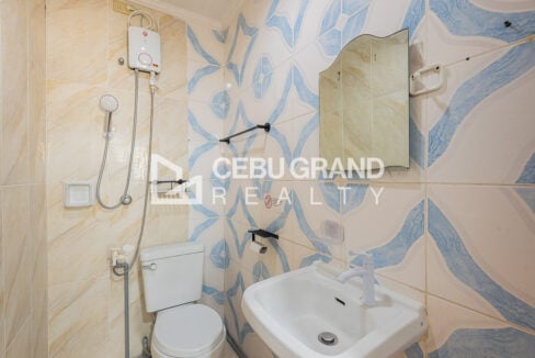 Bathroom with blue patterned tiles, a water heater and wall-hung mirror