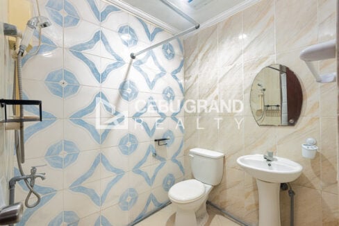 Shared bathroom in blue patterned tiles with a pedestal sink and shower rod
