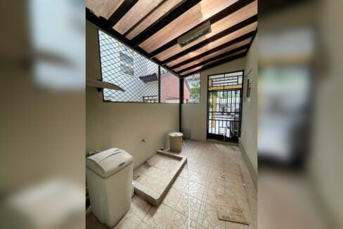 Covered laundry area with a wash basin, tiled floor and grilled door