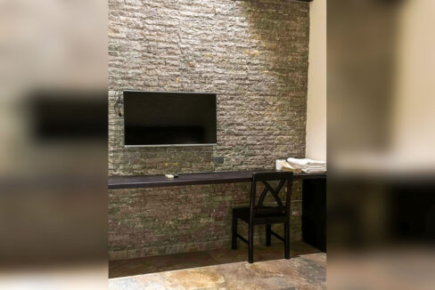 Guest room with a stone-clad feature wall, wall-mounted TV and built-in desk