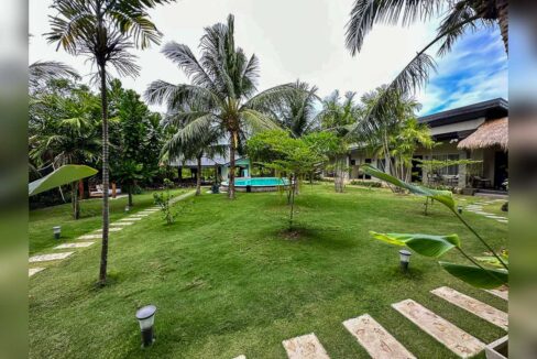 Wide lawn with coconut palms leading to the pool and restaurant pavilion at the Alcoy resort