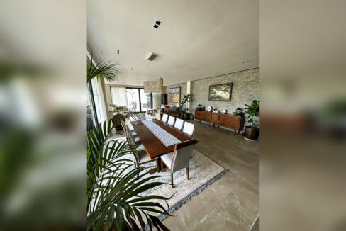 Ten-seat timber dining table under a woven pendant with a sideboard along the stone wall