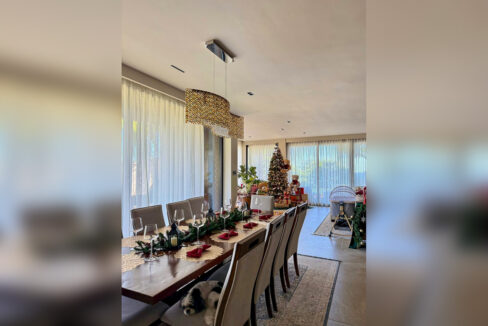 Dining table beneath a crystal pendant with sheer curtains over the glass doors