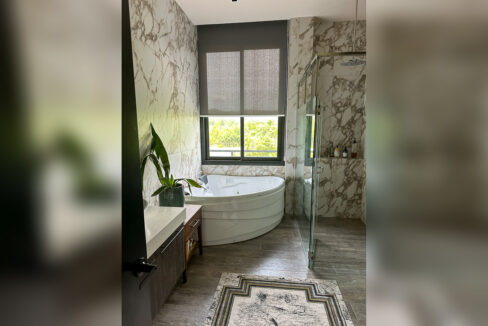 Master bath with a corner whirlpool tub, marble-look walls and glass rain shower
