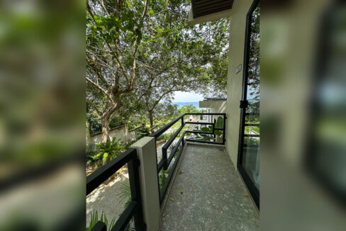 Terrazzo balcony with black steel railing looking through trees to the sea