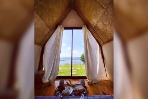 A-frame interior with woven bamboo walls and a glass door facing the lawn and sea