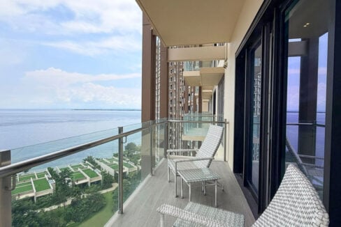 Balcony with glass railing and woven lounge chairs facing the sea at Aruga, Mactan