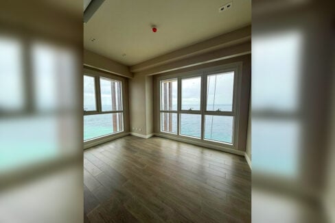 Corner bedroom with wood-look flooring and windows facing the open sea