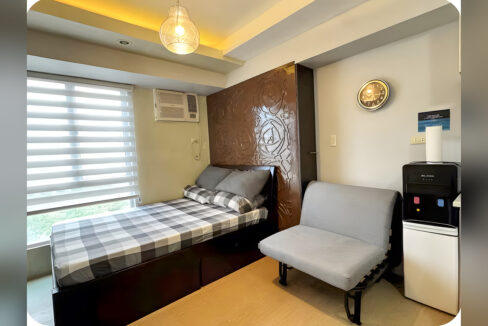 Bed with storage drawers, carved wood panel, sofa bed and window-type aircon in the Avida Tower 2 studio