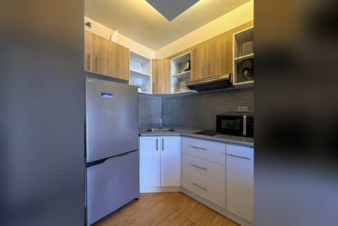 Kitchenette with wood-grain cabinets, grey mosaic backsplash, sink, microwave and two-door refrigerator