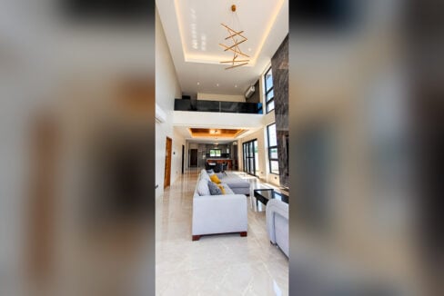Double-height living area with linear chandelier, cove lighting and glass mezzanine railing