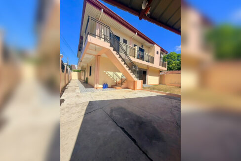 Paved driveway beside the house, with the stairway up to the second-floor walkway
