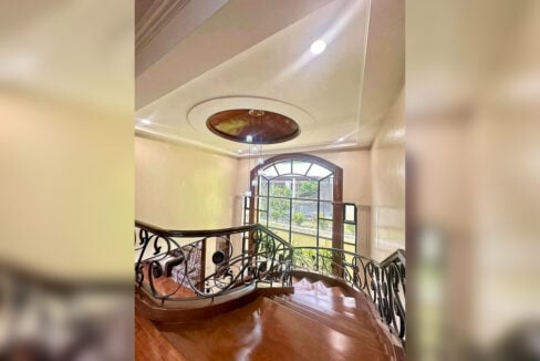 Curved staircase with wrought-iron railings and an arched window in the Banilad house