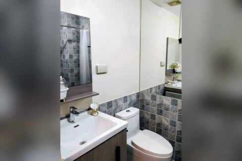 Bathroom with a wood-grain vanity, grey stone-look tiles and a mirror shelf