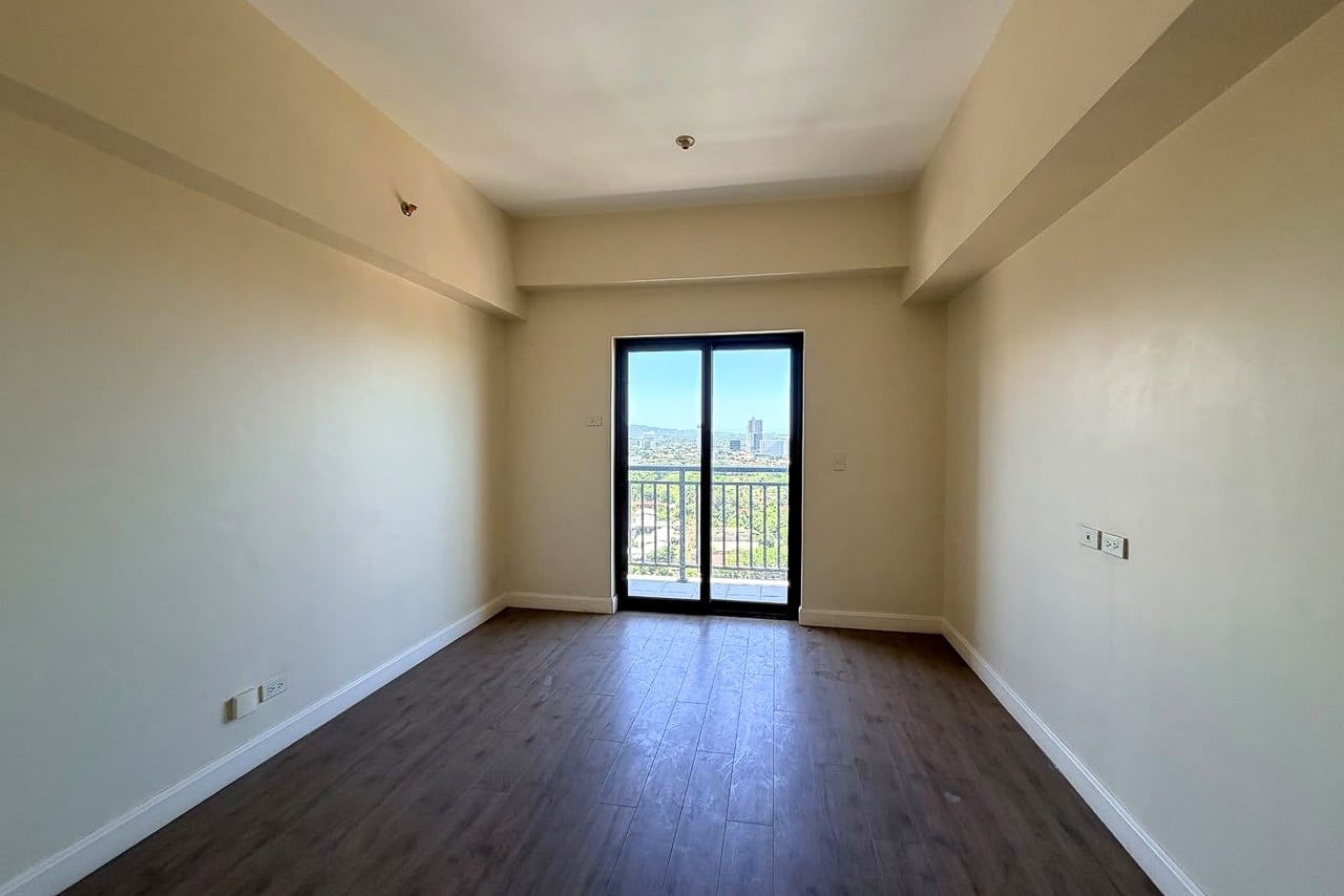 Empty studio room with wood-look floors and a glass door to the balcony at Grand Residences