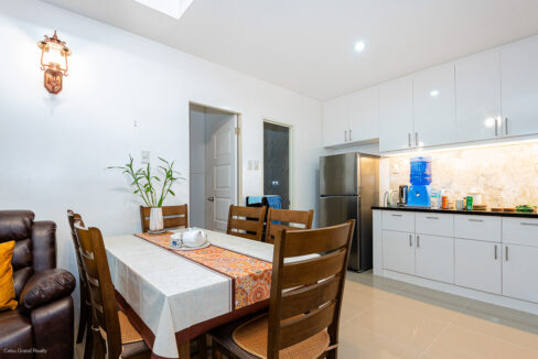 Dining table next to the kitchen with a two-door refrigerator and white gloss cabinets