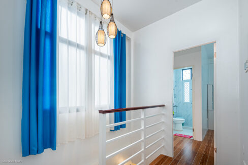 Upstairs landing at Ricksville Heights with blue curtains, rattan pendant lights and a white stair rail