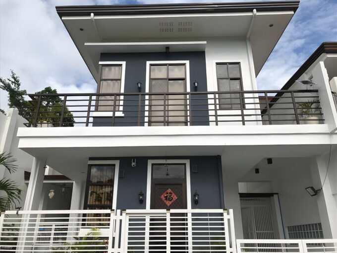 Front of the house with grey and white walls, dark balcony railing and wall lanterns