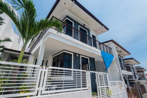 Corner view of the house behind a white slatted fence with a palm tree at the front