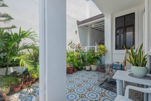 Side patio lined with potted plants under the covered walkway