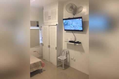 TV on a wall bracket, wall fan and tall white louvered cabinet