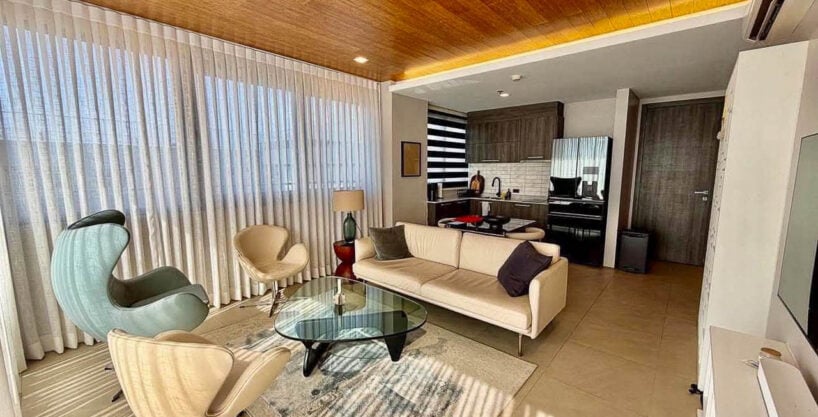 Living area with egg and swan chairs, cream sofa and wood-plank ceiling in a 2BR corner condo for sale at The Reef, Mactan
